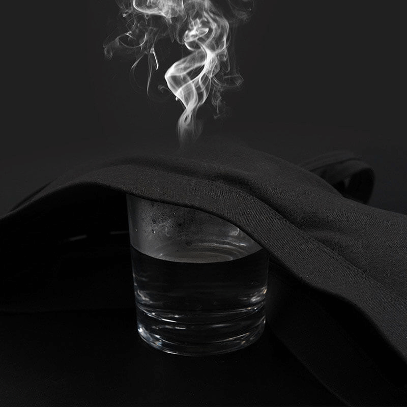 Steam rising from a glass of water under a black fabric, illustrating the breathability and quick-dry feature of the sports bra fabric.